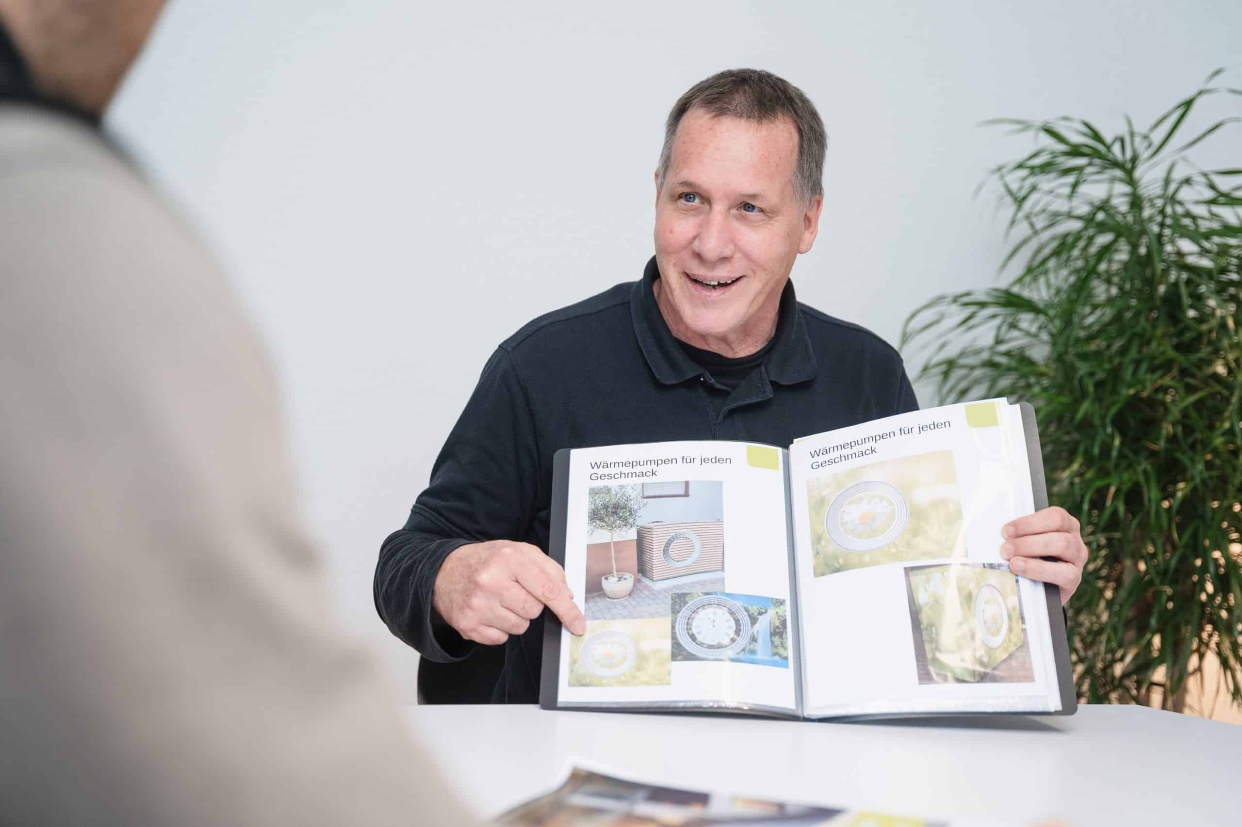 Peter Petrausch, Inhaber und Geschäftsführer bei FAENORA GmbH, zeigt einer Kundin den Katalog „Wärmepumpen für jeden Geschmack“