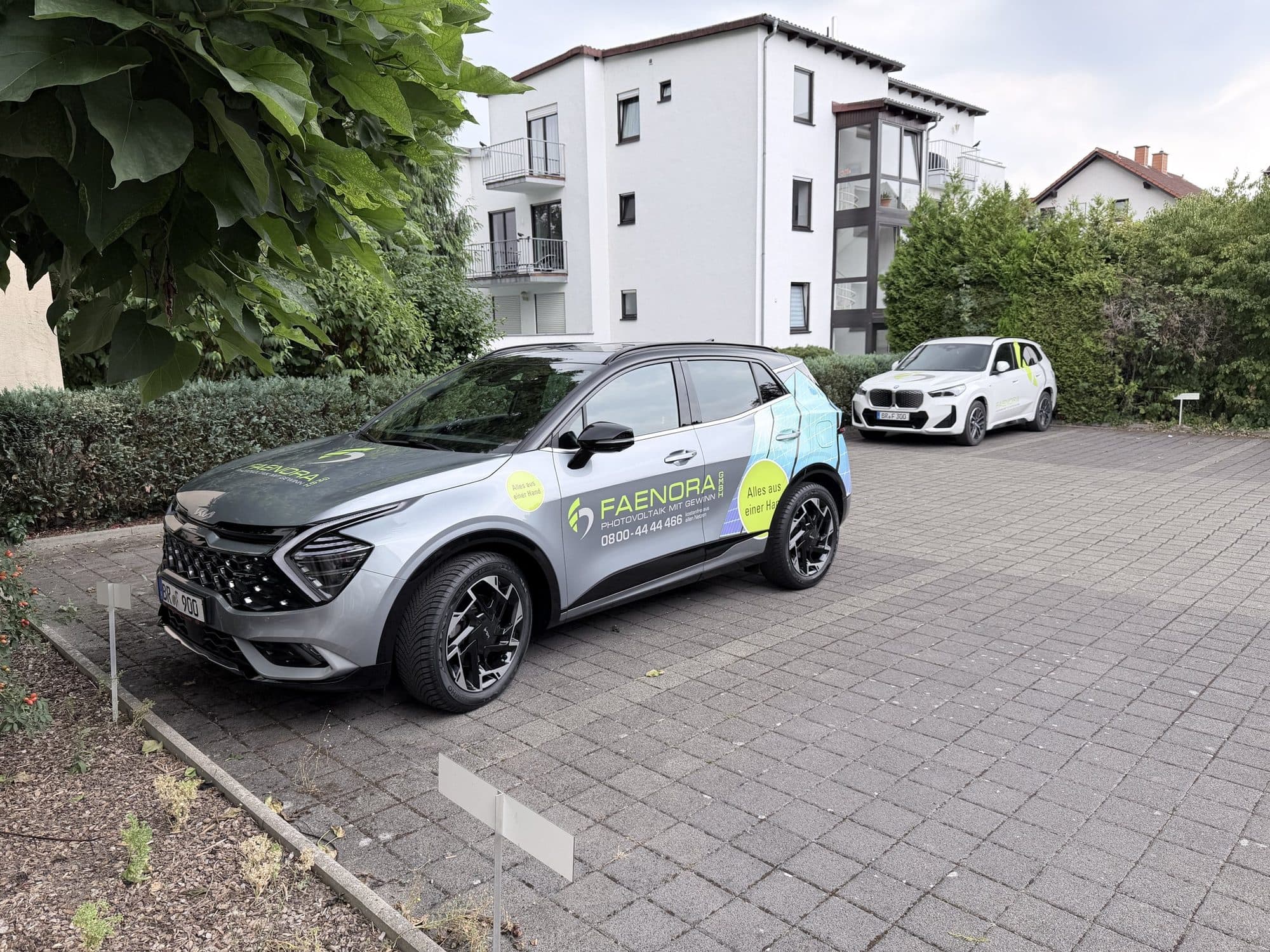 Silberner SUV mit FAENORA-Beschriftung auf einem Parkplatz vor einem Wohnhaus