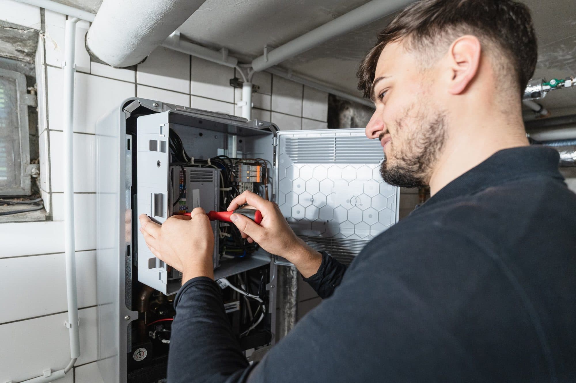 Monteur von FAENORA verdrahtet mit dem Schraubendreher das geöffnete Steuergerät einer Wärmepumpe im Technikraum